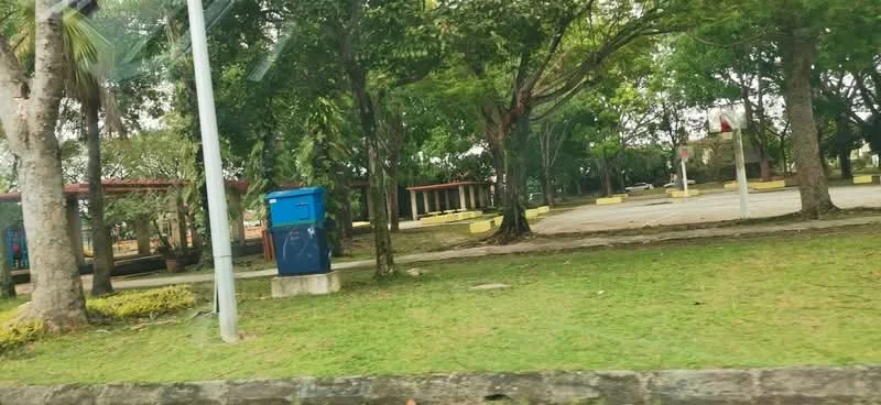 Exterior type: landscape garden; features: manicured lawn, mature trees, paved walkway, covered seating area, open space for activities, park benches, playground equipment, street lighting; style: tropical-modern.