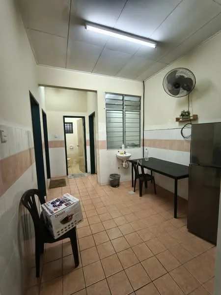 Room features: tile flooring, white painted walls, ceiling fan, single-basin sink, stainless-steel fridge, black dining table, plastic chair, laundry basket, doorway leading to bathroom, window with metal grilles.
