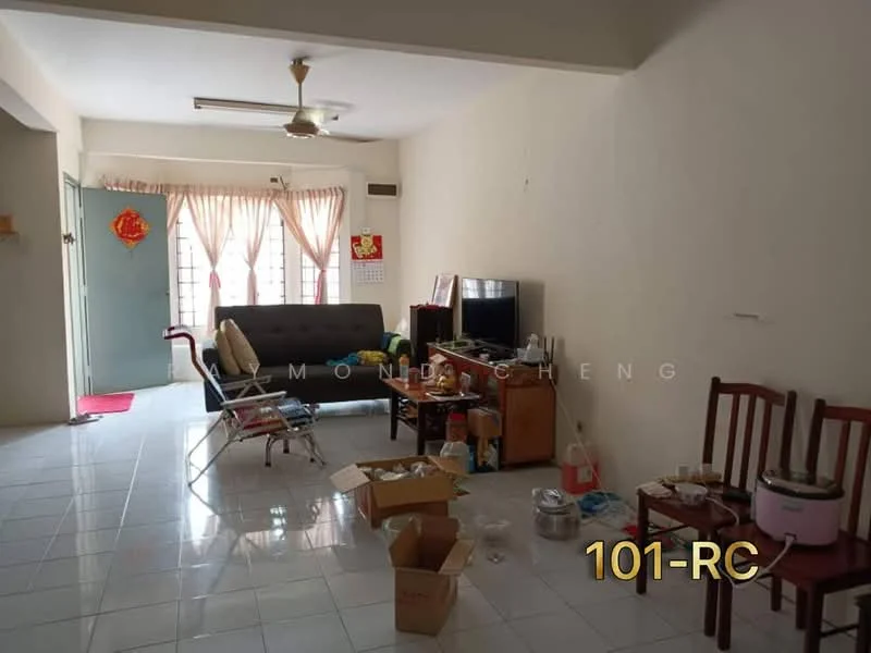 Living features: white painted walls, glossy ceramic tile flooring, 5-blade ceiling fan, sofa in grey, TV console, wall-mounted TV, coffee table, two wooden chairs, decorative wall calendar, large windows with sheer curtains, cardboard boxes, various kitchen items on the floor.