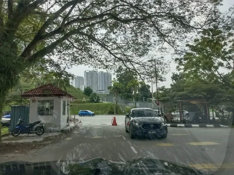 Exterior type: gated community entrance; features: guard house at entrance, boom gate, surrounded by mature greenery, paved driveway, security checkpoint, multi-storey buildings in background; style: modern.