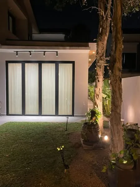 Exterior features: glass sliding doors with sheer curtains, landscaped garden with grass, decorative garden lights, potted plants, exterior wall lighting, trees in garden, stone pathway, modern architectural design; style: modern.