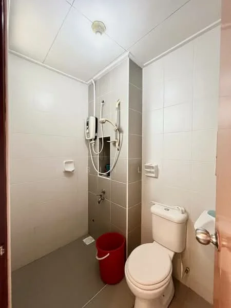 Bathroom features: white tiled walls, grey tiled flooring, shower area with wall-mounted showerhead, toilet, red bucket, water heater, soap holder, towel rack, light fixture on ceiling.
