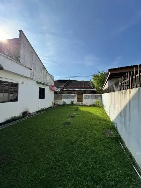 Exterior type: detached bungalow; features: manicured lawn, fenced yard, concrete wall, single-storey building, clear blue sky, adjacent buildings visible, garden area, pathway, greenery; style: modern.