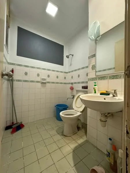 Bathroom features: white tiled walls, grey accent wall, white ceramic floor tiles, toilet, sink with chrome faucet, mirror, shower head, cleaning supplies, blue plastic bucket.