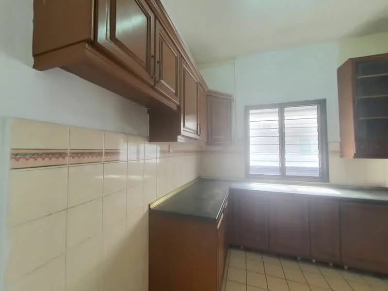 Kitchen features: brown wooden cabinetry, black countertop, white tiled walls, decorative border tile, single window with horizontal slats, ceramic tile flooring, corner layout, built-in storage cabinets.