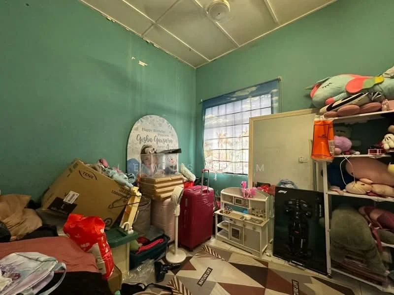 Room features: green painted walls, vinyl flooring, ceiling fan, window with sheer curtains, various plush toys, stacked boxes, luggage, shelves with toys and items, decorative wall sign.