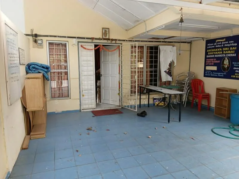 Room features: blue tiled flooring, white painted walls, metal grilles on windows, double doors, wooden cabinets, plastic table, stackable metal chairs, red plastic chair, decorative wall hanging, ceiling with exposed beams.
