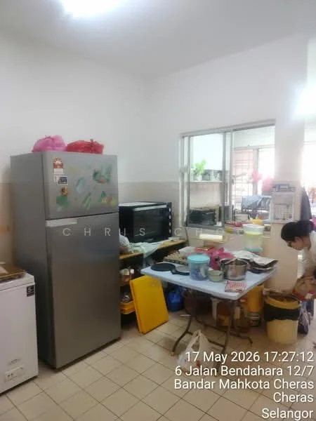 Kitchen features: stainless-steel fridge, white countertop, black microwave, white cabinets, yellow plastic containers, various cooking utensils, tile flooring, window with natural light, sink, table with multiple items.