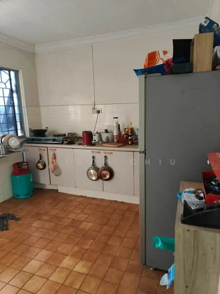Kitchen features: white tiled walls, brown tiled flooring, stainless-steel sink, chrome faucet, kitchen cabinets with wood finish, countertop with cooking stove, hanging pots, refrigerator, various kitchen appliances, window with metal grille, open shelving, kettle, red gas cylinder.