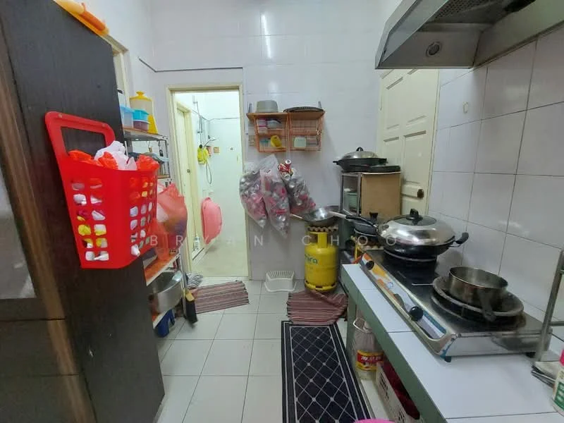 Kitchen features: white tiled walls, grey tiled flooring, stainless-steel gas stove, stainless-steel cooking pots, black countertop, wooden cabinets, red plastic basket, hanging storage rack, yellow container, sink with faucet, wall-mounted shelves, doorway leading to another room.