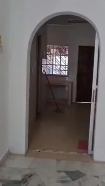 Room features: arched doorway, white painted walls, tile flooring, window with grid pattern, wooden door, cleaning broom visible, neutral color scheme.