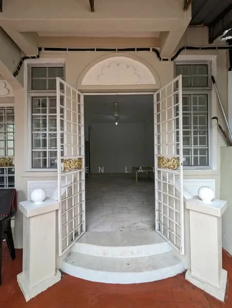 Exterior type: linked terrace house; features: double-door entrance with decorative grille, white painted facade, stone steps leading to entrance, two decorative pillars at entrance, red tiled flooring at entrance, ceiling fan visible inside, large windows with grille, open space visible beyond entrance; style: traditional.
