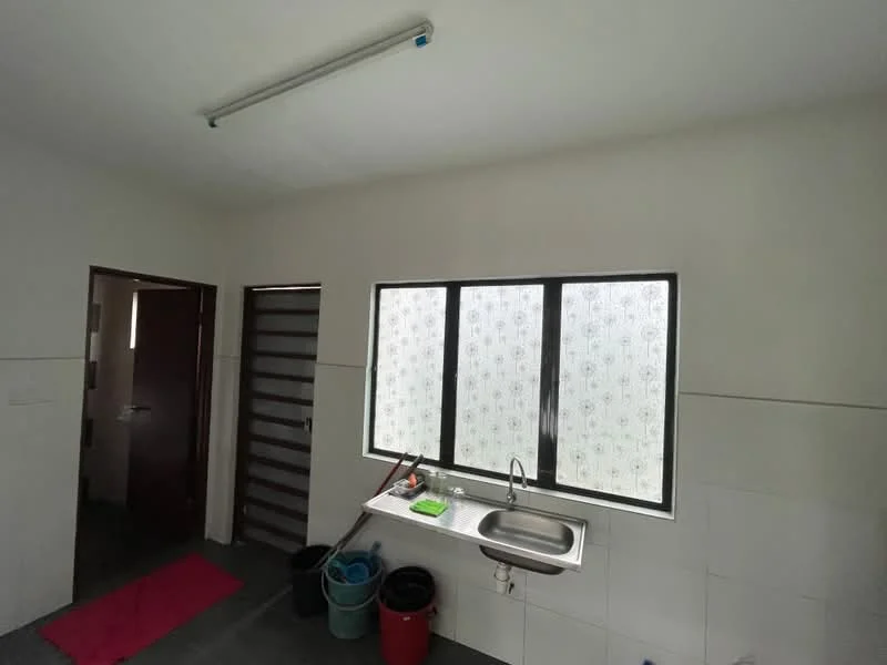 Room features: white painted walls, grey tiled flooring, single-bowl stainless-steel sink, chrome faucet, window with patterned glass, 2 plastic buckets, pink mat, door with horizontal slats.