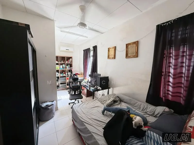 Bedroom features: white painted walls, tile flooring, 5-blade ceiling fan, queen-size bed with grey bedding, black office chair, wooden desk with computer, built-in wardrobe, bookshelf with various items, two windows with black curtains, decorative wall frames, stuffed animal on bed, laundry basket.