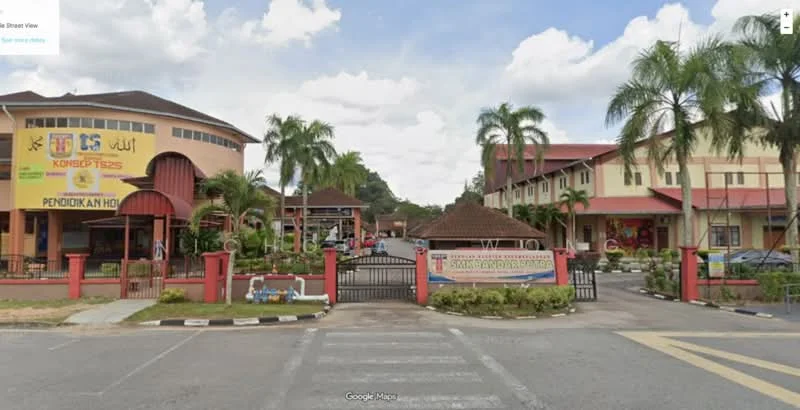 Exterior type: low-rise apartment block; features: gated entrance, paved driveway, landscaped garden with palm trees, two-storey building, signage at entrance, red brick facade, covered walkway, parking area, surrounded by greenery; style: modern.