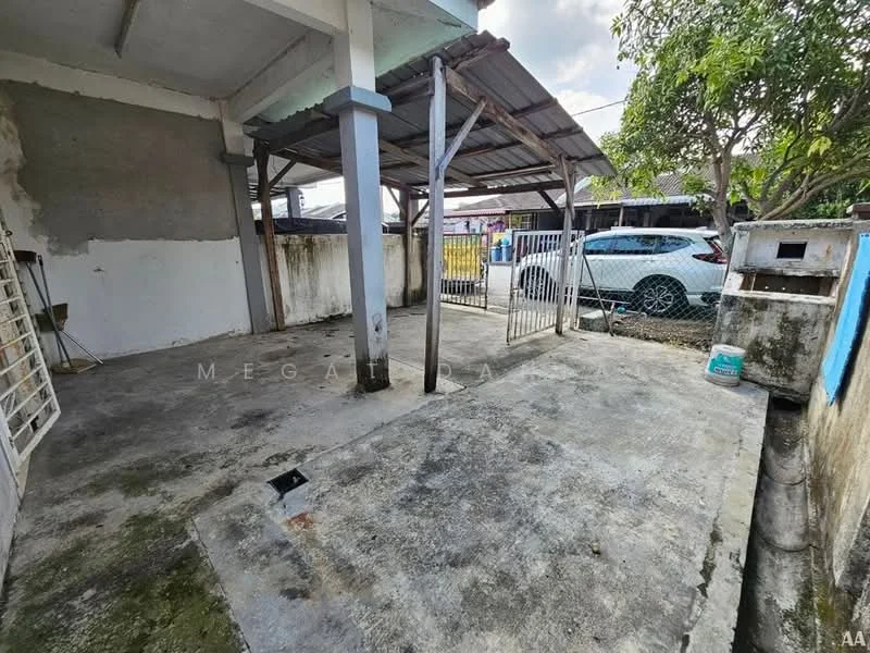 Exterior type: car porch; features: concrete flooring, metal roof, supporting columns, fenced area, open space, surrounding greenery, adjacent driveway, wall with paint peeling, utility area, visible car, gated entrance; style: minimalist.