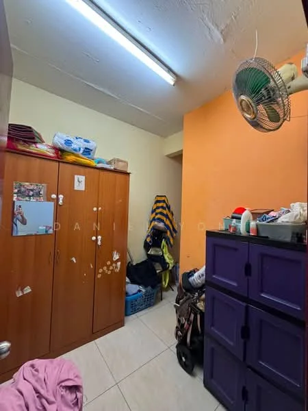 Room features: orange painted wall, white ceiling, fluorescent ceiling light, wooden wardrobe with multiple doors, purple storage cabinet, tile flooring, laundry basket, clothes hanging on a hook, ceiling fan, various items on shelves.