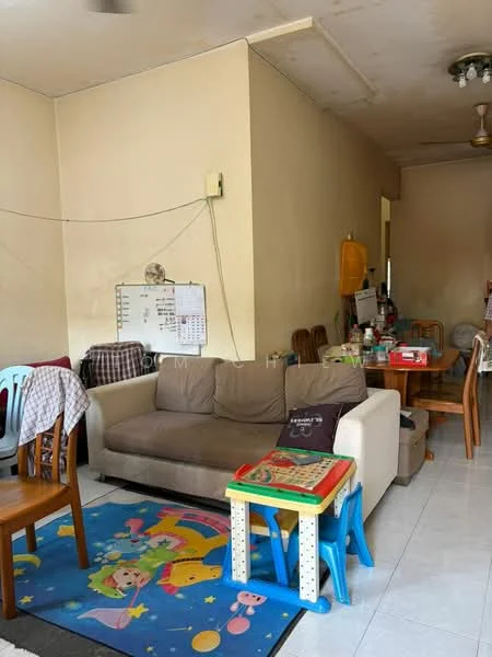 Living features: beige fabric sofa, wooden dining table, plastic stools, colorful area rug with cartoon design, white tiled flooring, ceiling fan, wall-mounted board, light yellow painted walls, wooden dining chairs, various items on table.