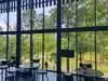 Room features: large floor-to-ceiling windows, views of greenery, modern furniture, tables and chairs, open space, natural light, polished concrete flooring, minimalist decor; style: modern; view: garden.