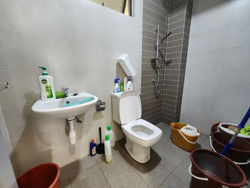 Bathroom features: white ceramic toilet, single-sink vanity with glass countertop, chrome basin mixer faucet, shower with handheld shower head, grey tiled walls, light grey floor tiles, cleaning supplies visible, plastic storage buckets, wall-mounted shower caddy; style: modern.