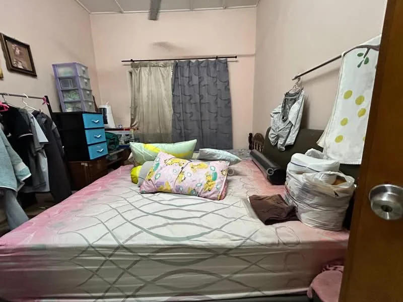 Bedroom features: queen-size bed with pink bedding, wooden headboard, two bedside pillows, decorative throw pillows, grey curtains, sheer curtains, clothes hanging on rack, black dresser with multiple drawers, plastic storage unit, wooden flooring, wall-mounted mirror, wall art or framed picture.