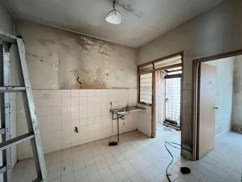 Kitchen features: white tiled walls, grey stained walls, white tiled flooring, single-bowl stainless-steel sink, wall-mounted faucet, window with metal grille, door leading to outdoor area, ceiling light fixture, ladder in the corner.