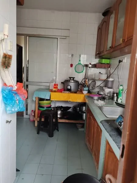 Kitchen features: white tiled walls, green laminate countertop, wooden cabinetry, stainless-steel sink, single-bowl sink, chrome faucet, electric rice cooker, plastic storage containers, stool, kitchen utensils, open shelving, floor tiles in light blue, window with sliding glass door.