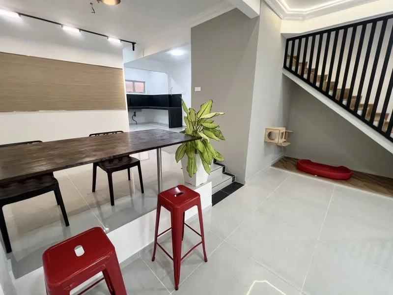 Room features: grey painted walls, white ceiling with crown moulding, tile flooring in light grey, wooden staircase, open space layout, bar counter with wooden top, 2 red metal stools, green indoor plant, cat tree, red pet bed, black cabinetry in background, large window with natural light; style: modern.