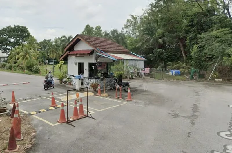 Exterior type: guard house; features: single-storey guard house, red tiled roof, white painted facade, wooden accents, security barriers, traffic cones, surrounded by greenery, paved driveway, parking spaces marked on ground; style: traditional.