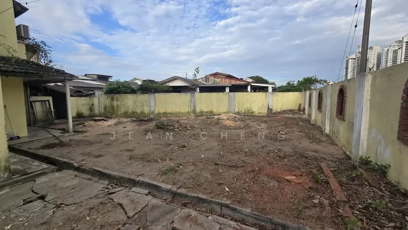 Exterior features: cleared land, fenced perimeter, concrete paving, overgrown vegetation, surrounding residential buildings, partially visible wall, open sky.