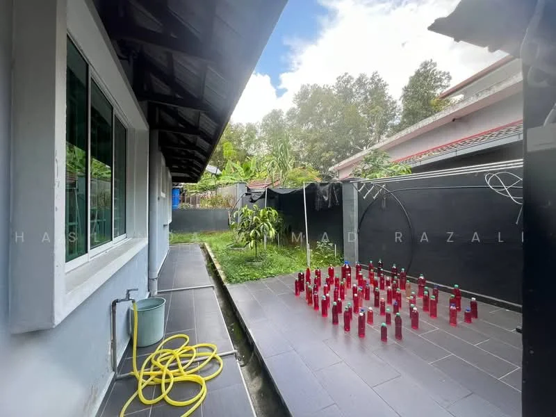 Exterior features: grey painted walls, black tiled flooring, manicured garden area, clothesline with hanging clothes, greenery in background, garden hose, water container.