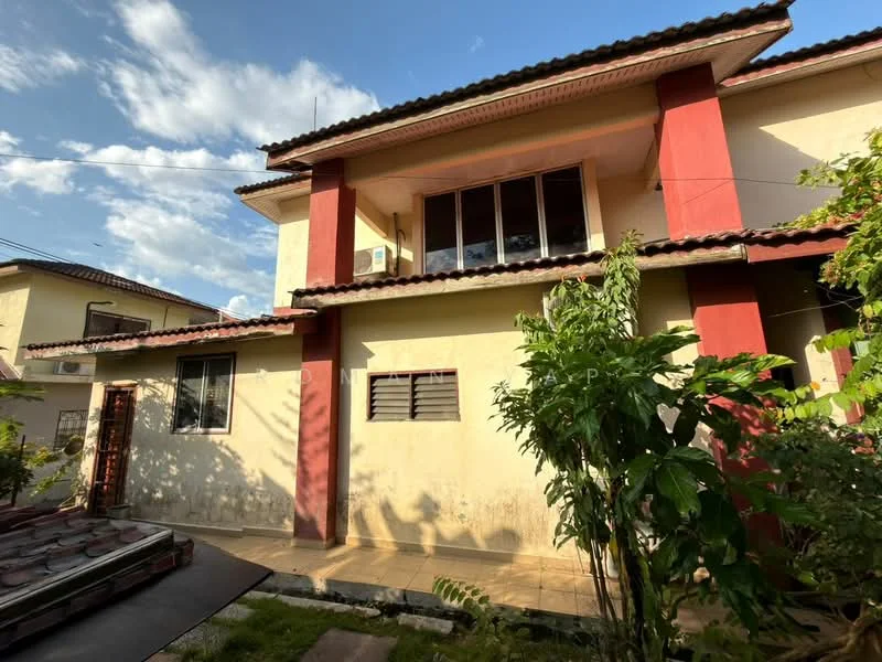 Exterior type: semi-detached house; features: yellow painted facade, red accent columns, flat roof, approximately 2-storey, manicured lawn, mature trees, windows with grilles, air conditioning unit visible, paved walkway, garden area; style: modern.