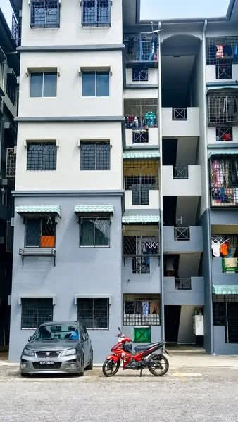 Exterior type: low-rise apartment block; features: grey painted facade, balconies with metal railings, ground-level parking area, visible laundry hanging on balconies, multiple storeys, windows with security grills; style: modern.