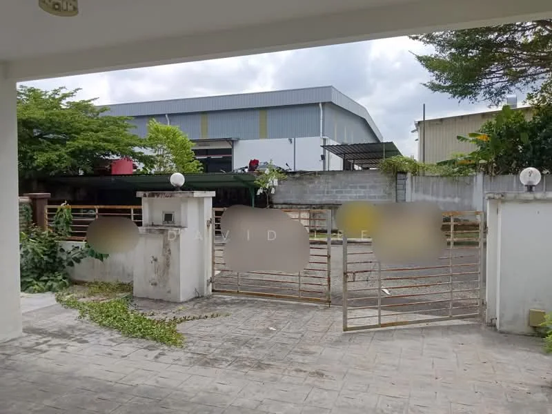 Exterior features: gate with metal bars, concrete wall, paved driveway, landscaped area with plants, surrounding greenery, industrial building in background, partially cloudy sky.