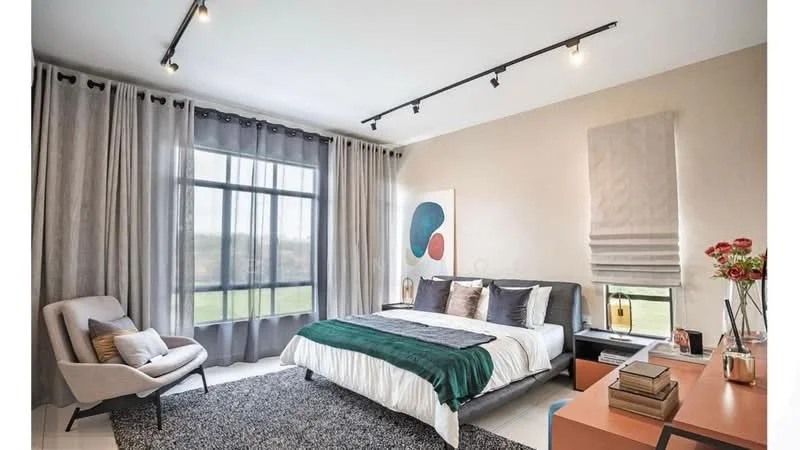 Bedroom features: king-size bed with green throw blanket, upholstered headboard, bedside lamps, large window with sheer curtains, blackout curtains, recessed LED downlights, track lighting, area rug with geometric pattern, wooden side table, decorative vase with flowers, accent chair in light grey, wall-mounted artwork; style: modern; view: garden.