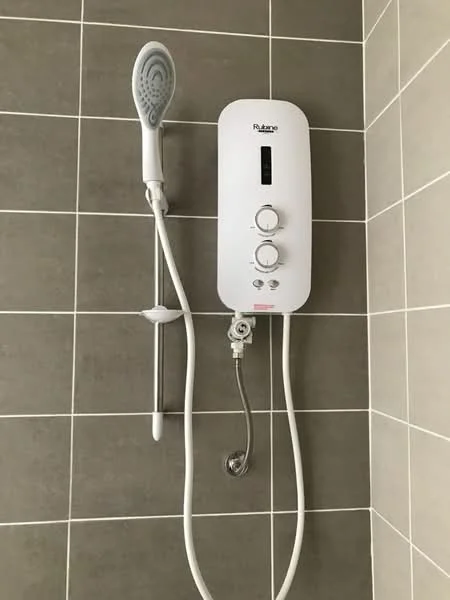 Bathroom features: white shower water heater, chrome showerhead, white shower hose, grey tiled walls, grey grout, wall-mounted controls; style: modern.