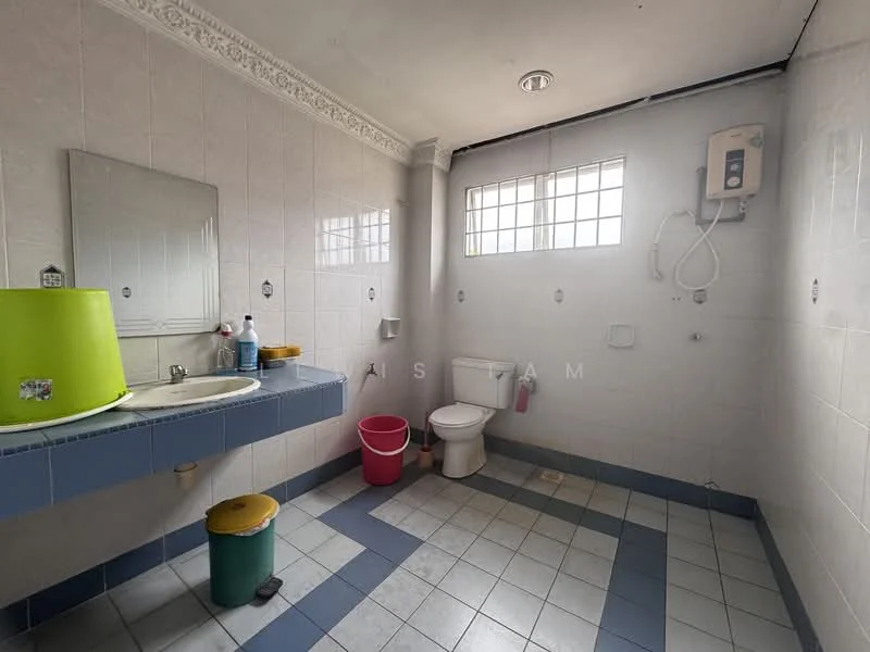 Bathroom features: white tiled walls, light grey tiled flooring, single-sink vanity with mirror, toilet, shower with wall-mounted water heater, window for natural light, green bucket, red trash bin, blue countertop, white wall-mounted fixtures.