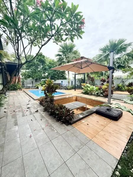 Exterior features: swimming pool, wooden deck, outdoor umbrella, landscaped garden, tropical plants, paved walkway, manicured lawn, patio area with seating, trees providing shade; style: tropical-modern.