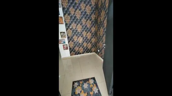 Room features: black and gold patterned wallpaper, cream tiled flooring, decorative wall art, doormat with geometric pattern, door with metallic finish; style: modern.