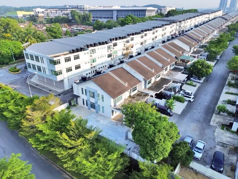 Exterior type: linked terrace house; features: two-storey linked terrace houses, brown pitched tile roofs, white painted facade, manicured landscaping with trees, driveway with interlocking pavers, open-air parking lot, surrounded by greenery, adjacent to a main road, multiple units in a row, visible car parking spaces; style: modern.