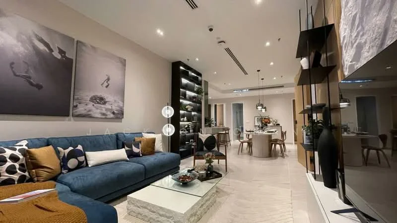 Living features: blue fabric sofa, decorative cushions with patterns, glass coffee table with stone base, wall-mounted TV, black shelving unit, framed artwork on walls, recessed ceiling lights, pendant lighting, dining area visible in background, wooden dining table, upholstered dining chairs, open-plan layout; style: modern.