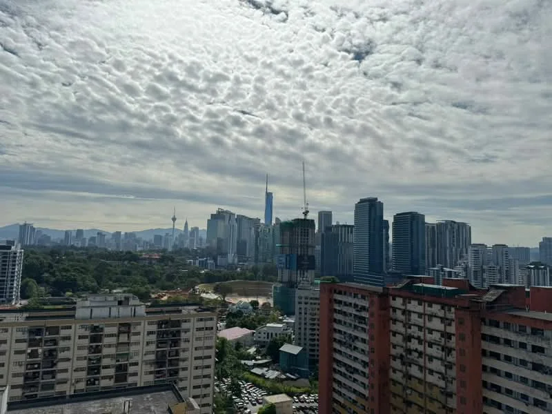 Exterior type: high-rise condominium; features: city skyline view, surrounded by urban landscape, visible construction site, various high-rise buildings, greenery in foreground, cloudy sky, Petronas Twin Towers visible, KL Tower visible; style: modern.