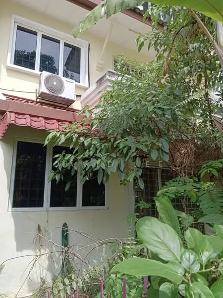 Exterior type: semi-detached house; features: red tiled roof, white painted facade, window air conditioning unit, multiple windows, greenery surrounding the house, overgrown plants in front, metal gate, brick wall, porch area; style: modern.