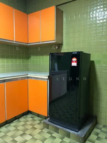 Kitchen features: orange cabinetry with flat-panel doors, white countertop, black fridge, green tiled walls, checkerboard vinyl flooring in green and yellow, overhead cabinets, sink area, wall-mounted electrical outlets.