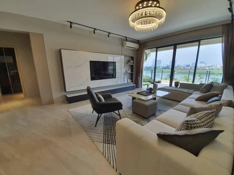 Living features: large sectional sofa in cream, black accent chair, coffee table with decorative items, area rug with geometric pattern, wall-mounted flat-screen TV, marble feature wall, floor-to-ceiling windows, curtains in neutral tones, recessed downlights, chandelier with crystals, light-colored marble flooring, decorative throw pillows; style: modern; view: city.
