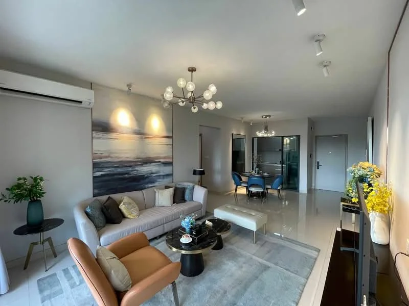 Living features: 3-seater fabric sofa in light grey, 2-seater armchair in tan, coffee table with black glass top, area rug with geometric pattern, chandelier with multiple bulbs, wall-mounted air conditioning unit, decorative wall art with abstract design, floor-to-ceiling windows, light grey painted walls, recessed downlights, TV console with decorative items, greenery in ceramic pot; style: modern. Dining features: round dining table, 4 upholstered dining chairs in blue, glass partition to kitchen, decorative flowers on table; style: modern.