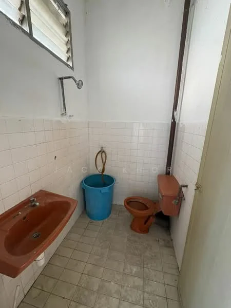 Bathroom features: orange ceramic sink, wall-mounted shower head, brown toilet, blue plastic bucket, white tiled walls, grey tiled flooring, window with horizontal slats.