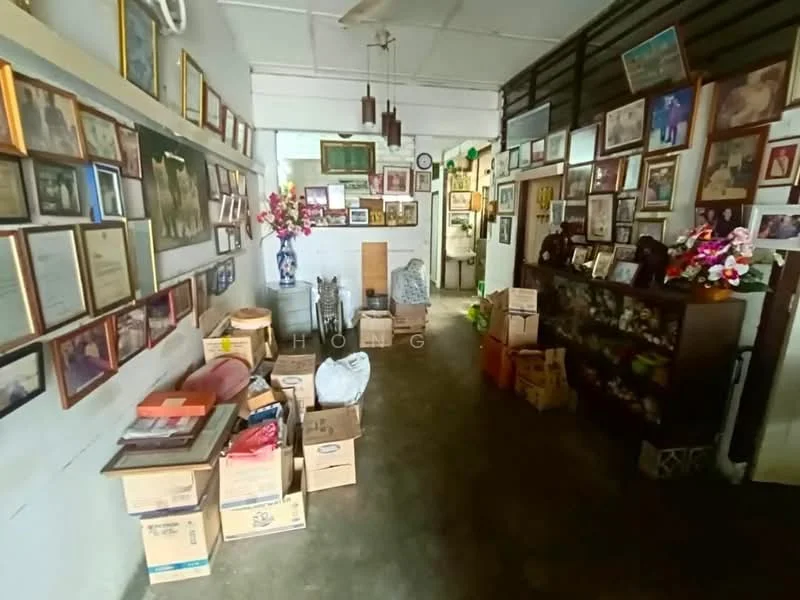 Room features: concrete flooring, white painted walls, various framed photographs on walls, decorative wall-mounted shelves, wooden sideboard, boxes stacked on the floor, artificial flowers in vases, hanging light fixtures, clock on the wall; style: traditional.