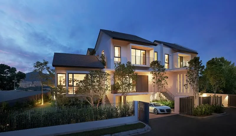 Exterior type: detached bungalow; features: white painted facade, pitched tile roof, double-storey, manicured lawn, mature trees, landscape lighting, driveway with interlocking pavers, gated entry, large windows, balconies with glass railings; style: modern.