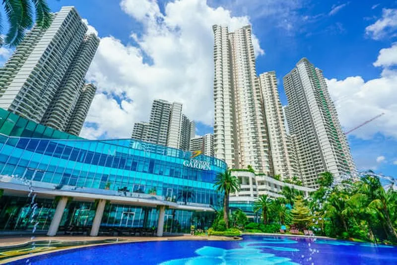 Exterior type: high-rise condominium; features: glass curtain wall facade, multiple high-rise towers, swimming pool with water features, lush tropical landscaping, manicured gardens, outdoor seating areas, palm trees, blue sky with clouds; style: modern.